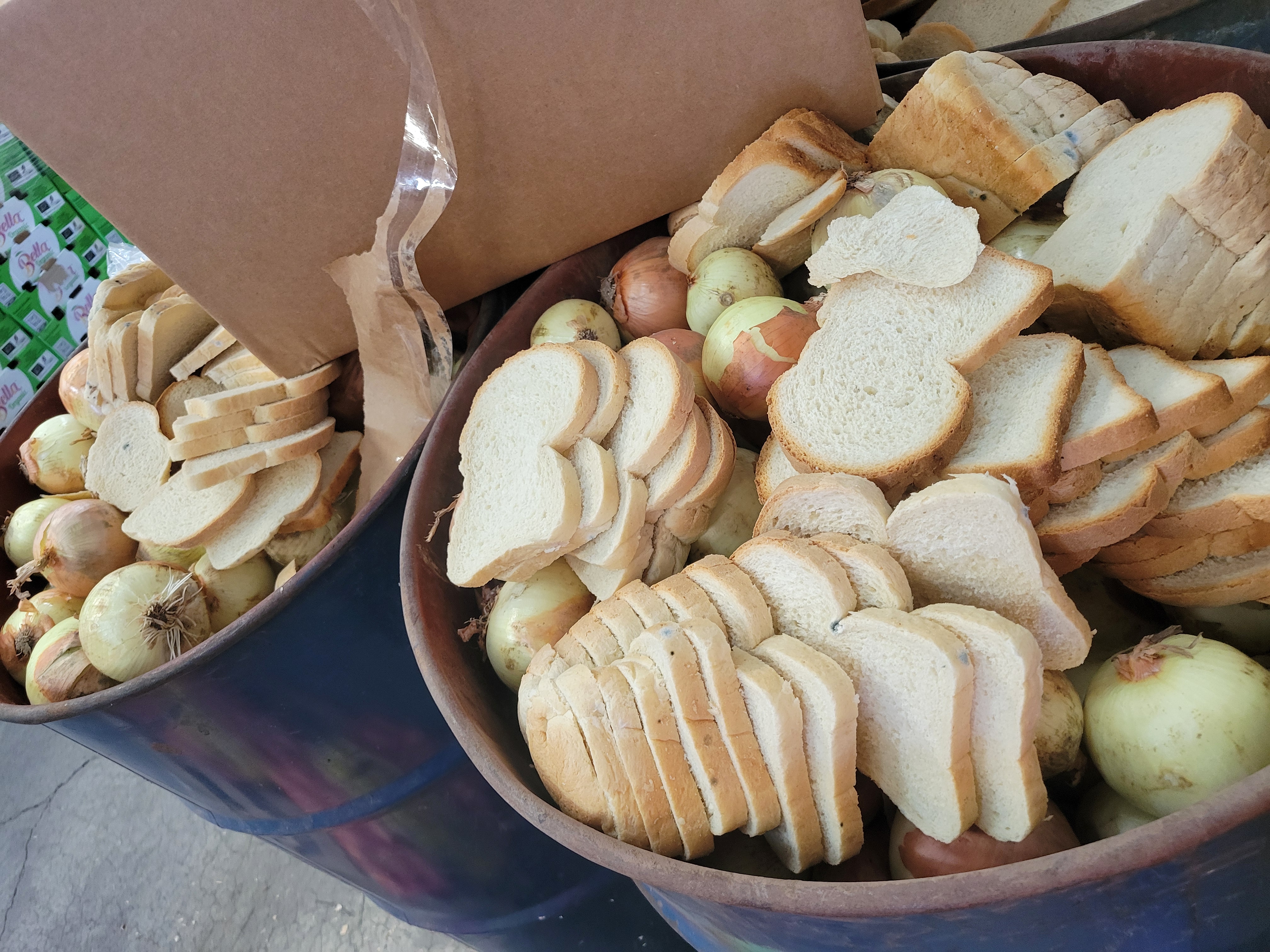 A collection of rotten food consisting of sliced bread and whole onions inside large containers.
